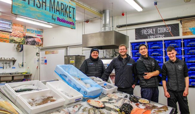 Four staff members pose at a fresh seafood market, surrounded by fish and seafood displays.