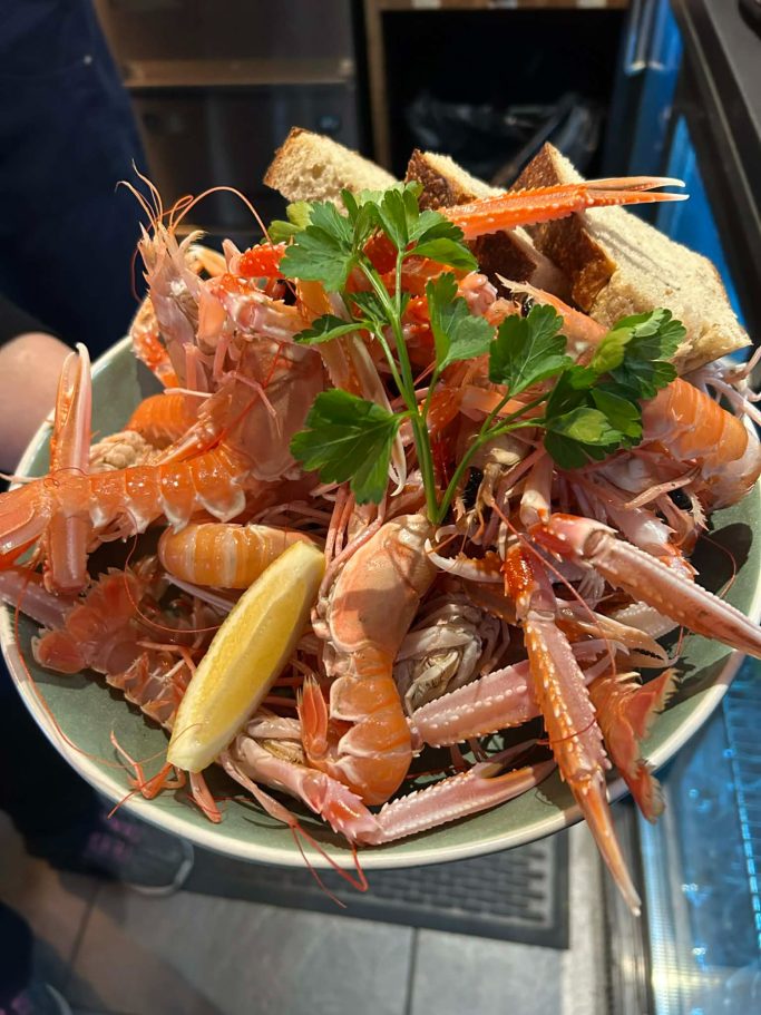 A seafood platter featuring shrimp, prawns, bread, and a slice of lemon, garnished with parsley.