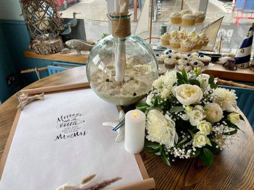 A vase with flowers, a candle, and a scroll on a table by a window.
