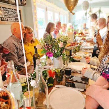 A lively dining scene with guests enjoying a meal decorated with flowers and balloons.