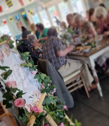 A lively gathering of people dining together, decorated with flowers and greenery.