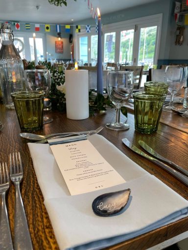 Table setting with green glasses, cutlery, a menu, and a blue candle in a restaurant.
