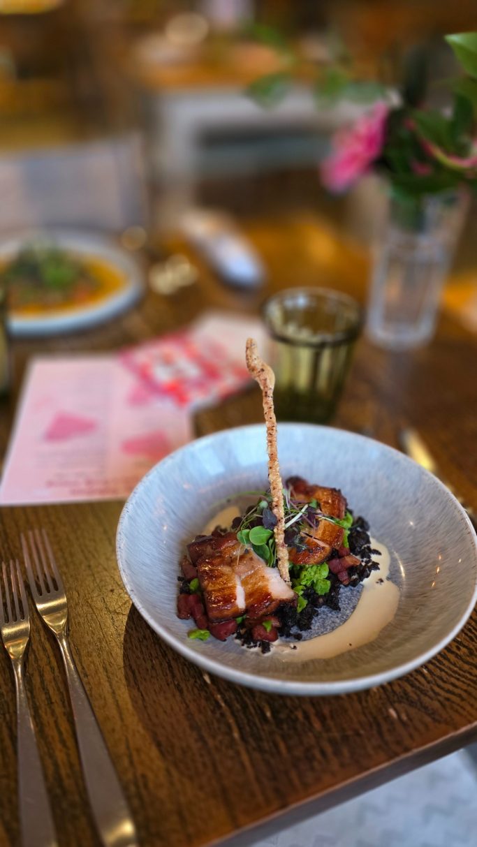 Plate of tender meat with garnishes on a wooden table, surrounded by a soft-focus background.